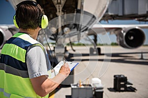 Airport worker looking at passenger plane and writing information