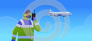 airport worker marshaller man communicating over walkie-talkie with air traffic control while airplane flying in sky photo
