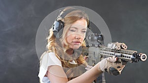 Airsoft female shooter holding an automatic assault rifle and aiming at enemy.