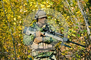Airsoft man in uniform hold sniper rifle on yellow forest backdrop. Side view photo