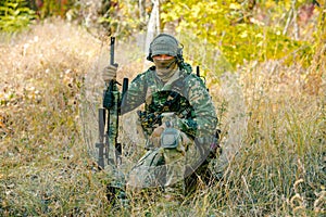 Airsoft man in uniform with sniper rifle, lurking in grass on forest background. Front view photo