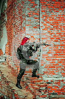 Airsoft red-hair woman in uniform with machine gun beside brick wall. Soldier aims at the sight on the ruins. Vertical photo side photo