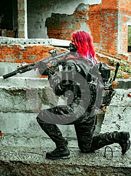 Airsoft red-hair woman in uniform with machine gun standing on knee. Soldier on ruine. Vertical photo side view photo