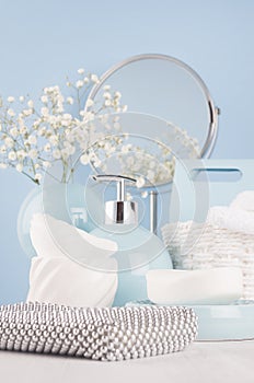 Airy blue dressing table with cosmetic accessories, mirror, basket, towel, silver bag, flowers and ceramic bowls on white wood.