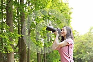 Aisan Chinese woman photographer hold camera close to her face work in nature shot maple green plants