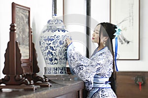 Aisan Chinese woman in traditional Blue and white Hanfu dress, stand by a ancient table.