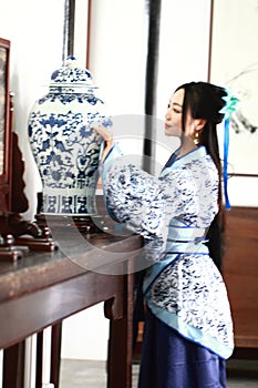 Aisan Chinese woman in traditional Blue and white Hanfu dress, stand by a ancient table.