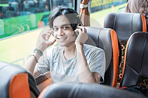 a aisan man wearing headphones smiles while listening to music while sitting by the window photo