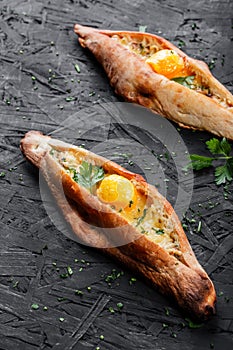 Ajarian Khachapuri traditional Georgian cheese pastry with eggs on dark wooden background.