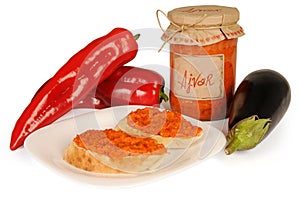 Ajvar - delicious dish of red and green peppers, onions, garlic, eggplant. Ajvar in jar. Sauce spread on two slices of bread on pl