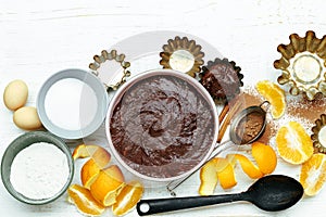 Aking ingredients of chocolate cake with orange peel, cinnamon and kitchen utensil on white wooden table