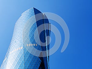 Al Bidda Tower against clear blue sky, close up. Modern skyscraper with glazed facade
