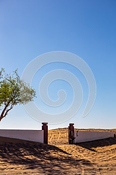 Al Madam ghost village, abandoned courtyard and brick fence with entry gate buried in sand in Sharjah, United Arab Emirates