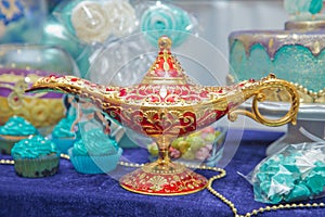 Aladdin lamp of wishes on table . Aladdin's magic genie lamp in red and gold on a blue background. Antique golden