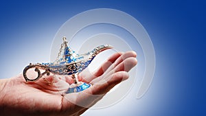 Aladdin`s magic lamp in a woman`s hand on a pale blue background. Arabian fairy tales, magic. Symbol of good luck, wealth.