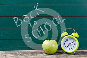 Alarm clock and apple on the green chalkboard with back to school text, education concept