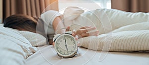 alarm clock and asian woman hand stop time in bed while sleeping, young adult female wake up late in the early morning. Relaxing
