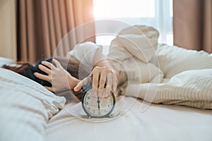 alarm clock and asian woman hand stop time in bed while sleeping, young adult female wake up late in the early morning. Relaxing