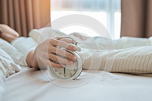 alarm clock and asian woman hand stop time in bed while sleeping, young adult female wake up late in the early morning. Relaxing