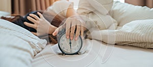alarm clock and asian woman hand stop time in bed while sleeping, young adult female wake up late in the early morning. Relaxing