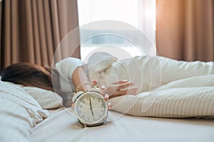 alarm clock and asian woman hand stop time in bed while sleeping, young adult female wake up late in the early morning. Relaxing