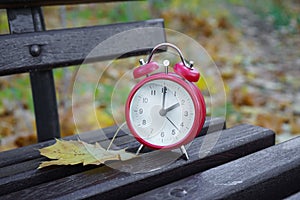 Alarm clock in autumn park on the bench. Passing of time and season change concept