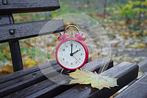 Alarm clock in autumn park on the bench. Passing of time and season change concept