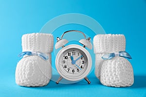 Alarm clock and baby booties on light blue background. Time to give birth