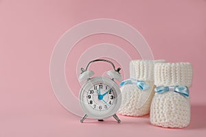 Alarm clock and baby booties on pink background, space for text. Time to give birth