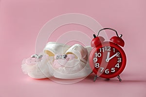 Alarm clock and baby booties on pink background. Time to give birth