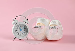 Alarm clock and baby booties on pink background. Time to give birth