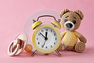 Alarm clock, baby dummy and toy bear on pink background. Time to give birth