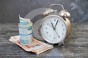 Alarm clock and Banknotes one and five thousand rubles in a cutlet of money tied with a rubber band close-up