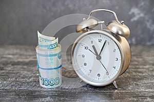 Alarm clock and Banknotes of one thousand rubles in a cutlet of money tied with a rubber band close-up