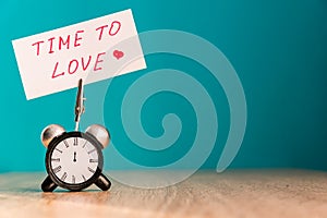 Alarm clock and banner with handwritten phrase`time to love` on wooden table. Time management concept.