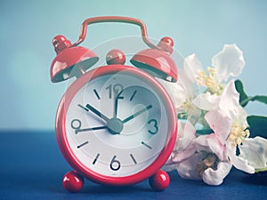 Alarm clock and beautiful spring flowers on blue table, space for text. Time change concept