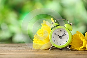 Alarm clock and beautiful spring flowers on table, space for text. Time change concept