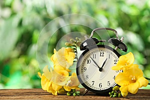 Alarm clock and beautiful spring flowers on table. Time change concept