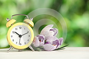 Alarm clock and beautiful spring flowers on  wooden table. Time change concept