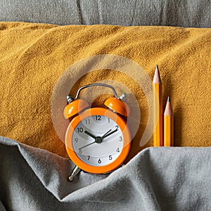 Alarm clock in bed on colored textiles. The concept of awakening, work time, training (studying), back to school.