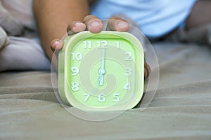 Alarm clock on the bed with hand of man in bedroom. Focus on hand with clock on brown bed. Wake-up time lifestyle concept