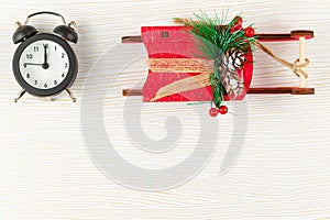 Alarm clock in a black case and red sleigh of santa claus on a white background with gold veins