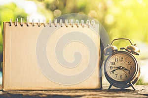 Alarm clock and blank calendar page on wooden background