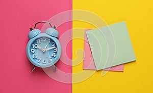 Alarm clock and blank reminder notes on color background, flat lay