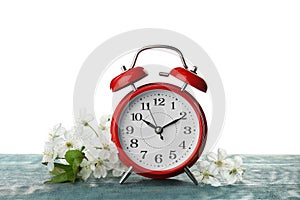 Alarm clock and branch with spring blossoms on wooden table against white background. Time change concept