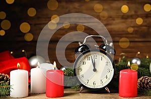 Alarm clock, burning candles and Christmas decor on wooden table, bokeh effect