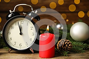 Alarm clock, burning candles and Christmas decor on wooden table, bokeh effect