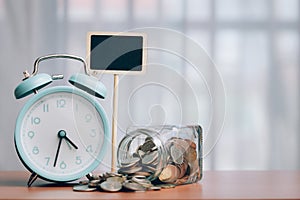 Alarm clock and coins with blank chalkboard on wood table with copy space