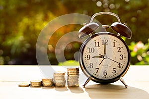 Alarm clock and coins with sunlight in the park Represents the beginning of saving money.