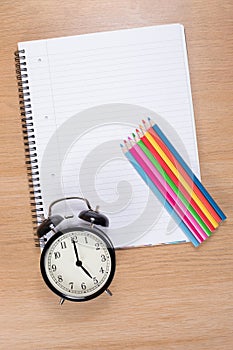 Alarm clock with colored pencils lying on notebook
